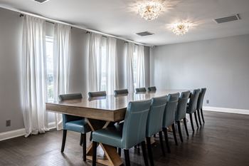 A long wooden table with blue chairs is in the middle of a room with a window